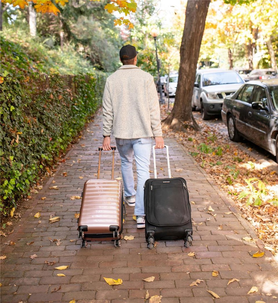 Ein Mann läuft mit zwei Koffern einen Weg entlang