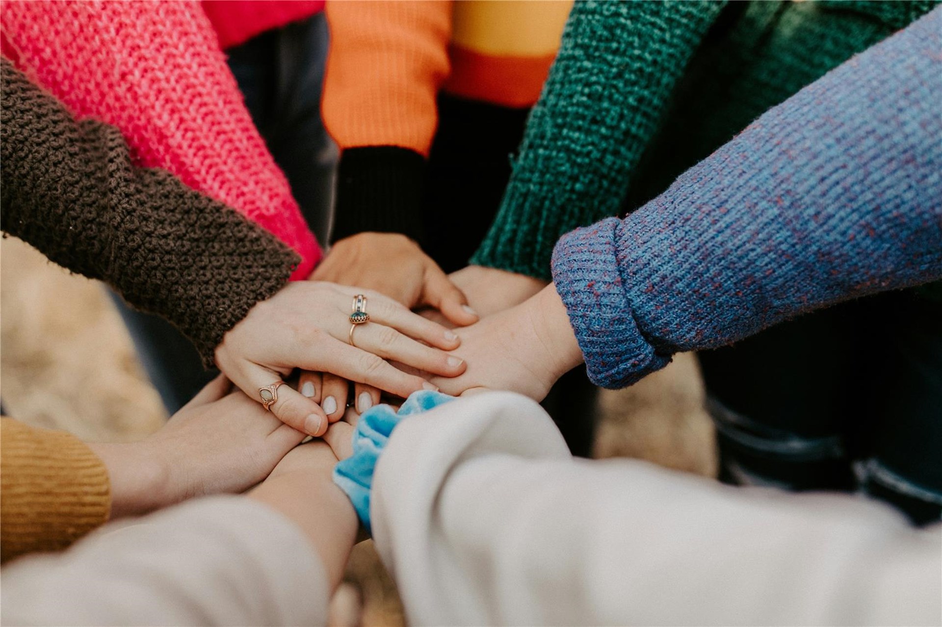 die Hände mehrerer Personen liegen in der Mitte übereinander. die Arme stecken und bunten Strickpullovern. Ein Symbol für die gemeinsame, unterstützende Arbeit