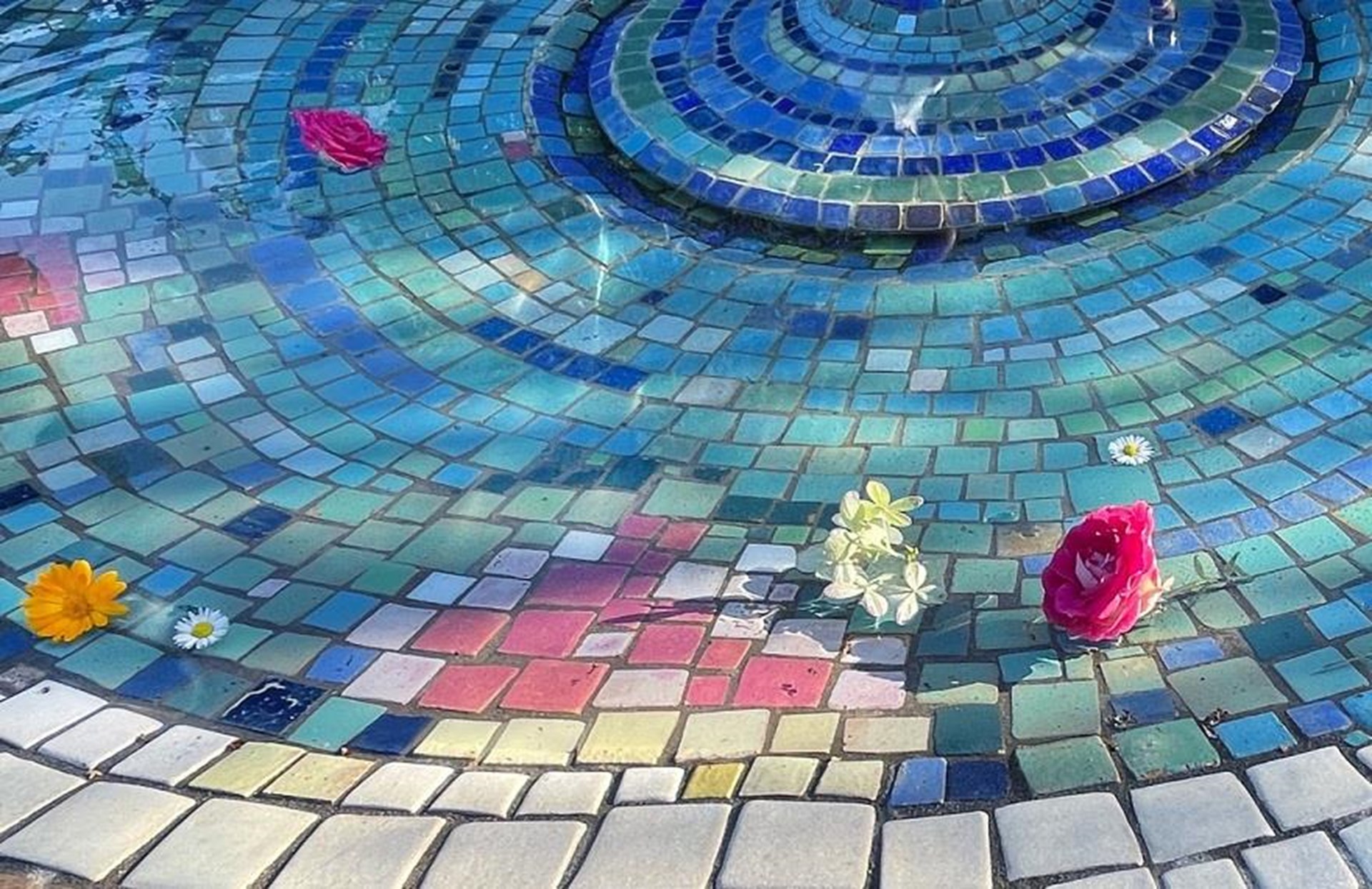 Detailansicht eines Brunnes im Mosaikstil mit vereinzelten, auf dem Wasser schwimmenden Blüten