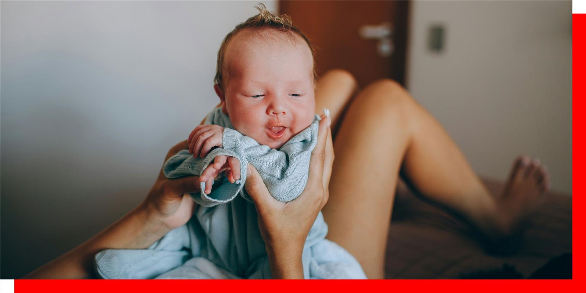 Lustiges Baby sitzt auf dem Bauch der jungen Mama